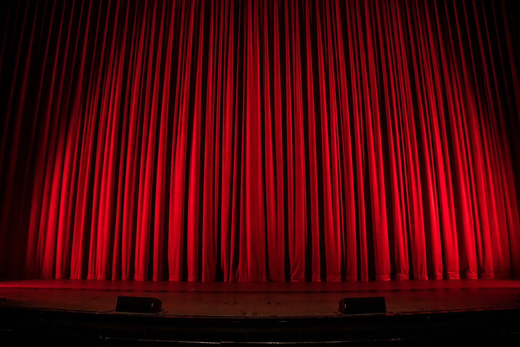 Red theatre curtains above an empty stage.